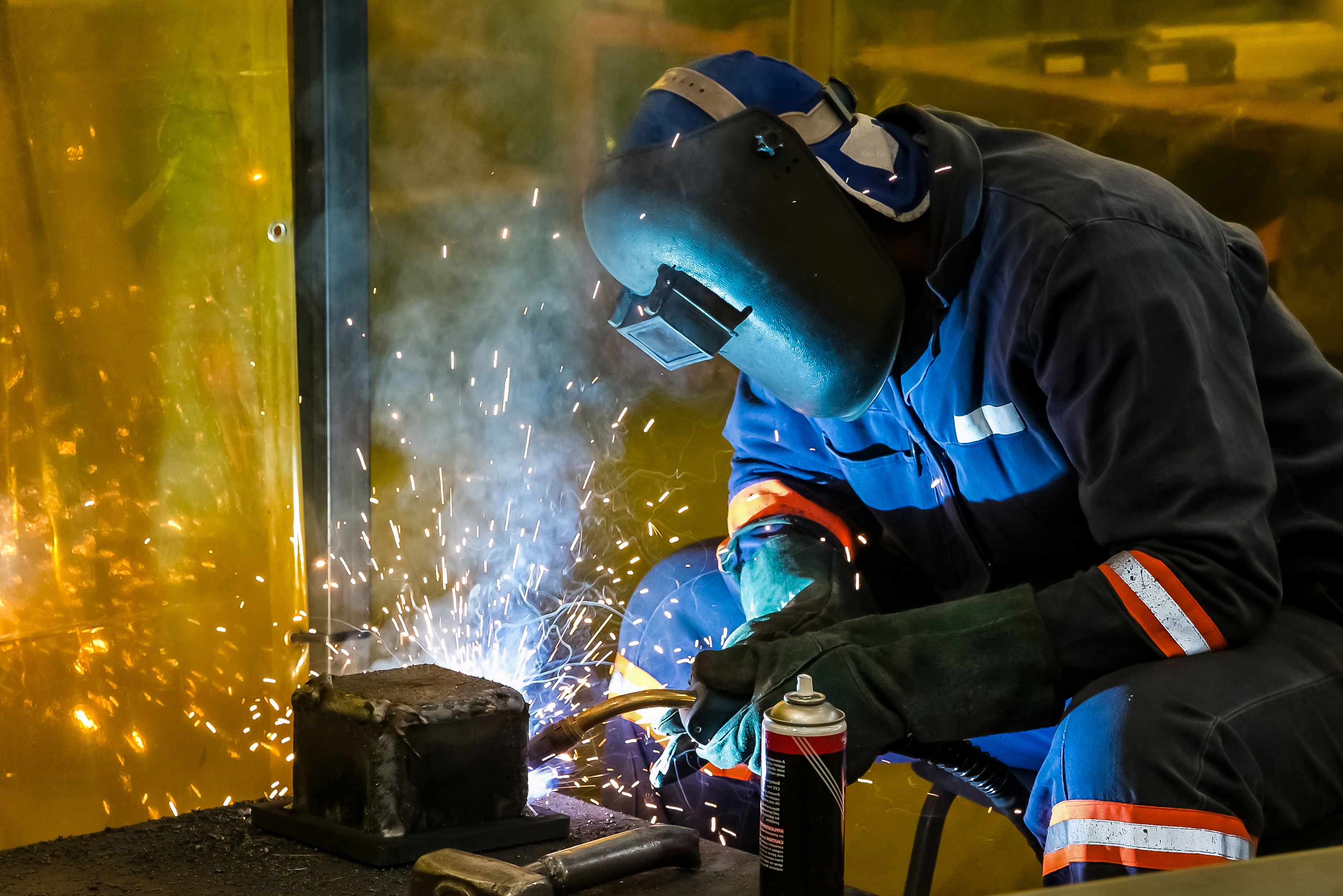A skilled welder wearing protective gear uses a torch to weld a metal joint in a workshop.